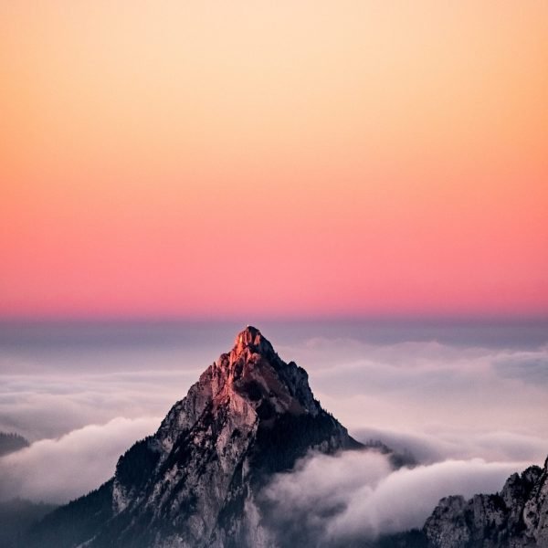 An aerial view of a mountain covered in fog under the beautiful pink sky